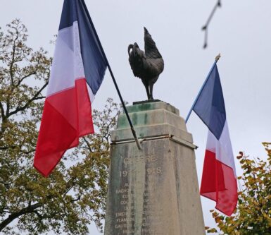 2 drapeaux autour d'un coq gaulois noir posé sur le haut d'un monument en pierre avec inscriptions gravées