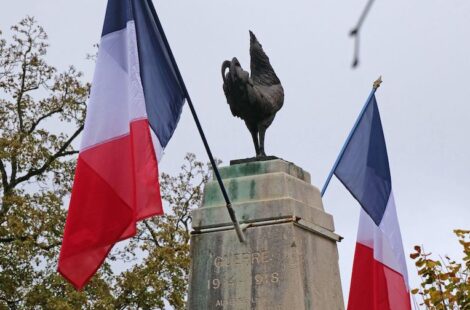 2 drapeaux autour d'un coq gaulois noir posé sur le haut d'un monument en pierre avec inscriptions gravées